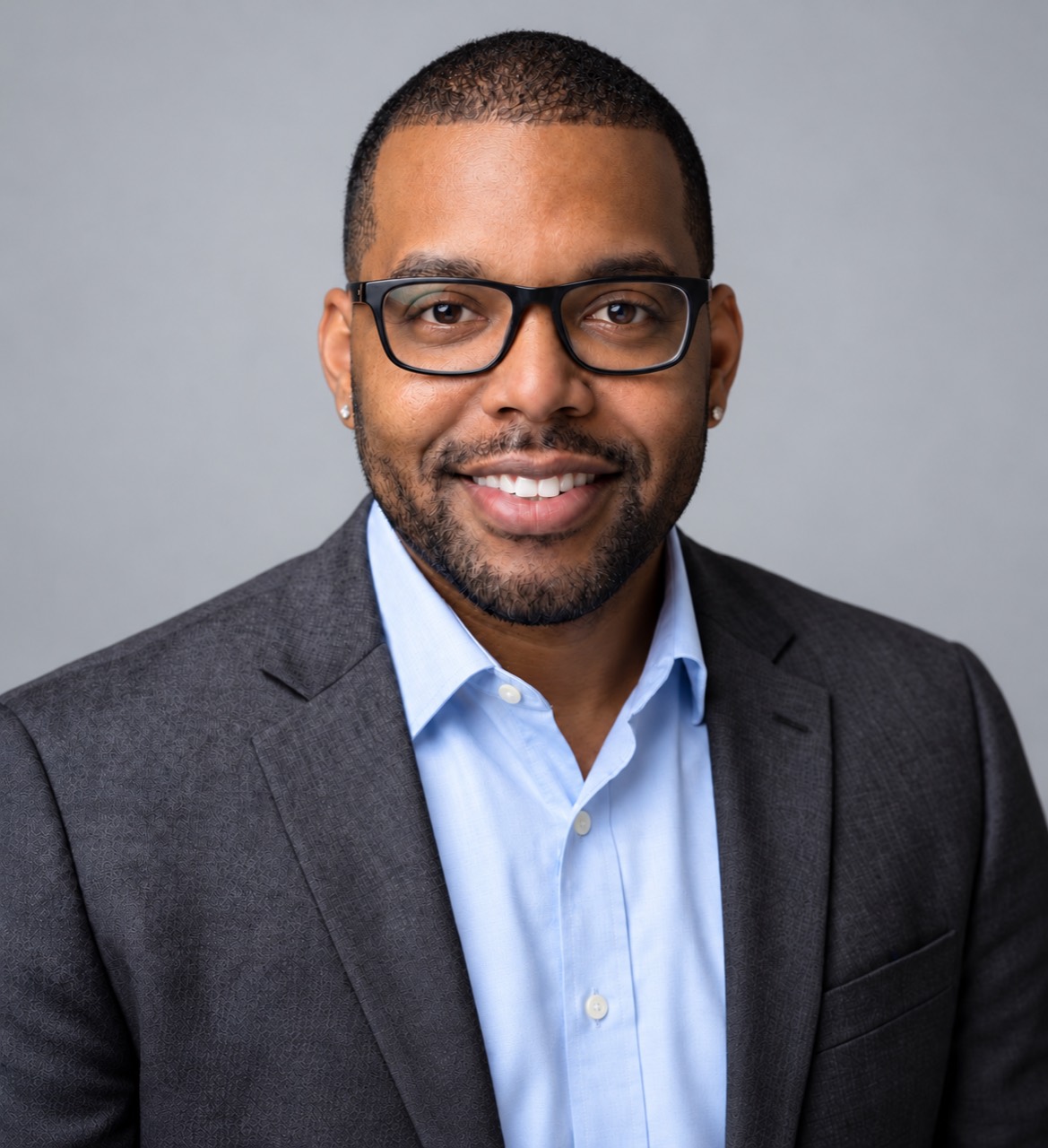 Dennis Griffin smiling in a dark blazer, light-blue shirt, and glasses